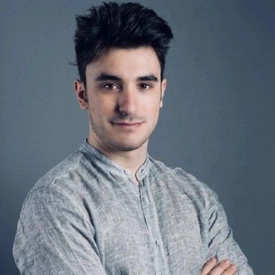 Nicholas Barsanti, sorridente, in camicia grigia e a braccia conserte